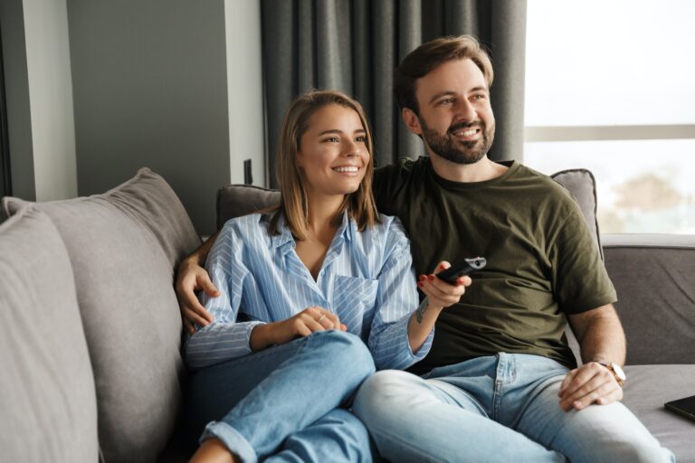 Photo of joyful couple watching TV and using remote control